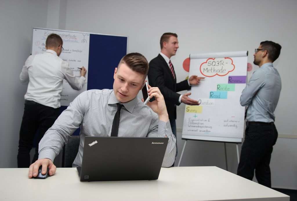 A Call Center Outsourcing representative on a call while his team discuss in the background.