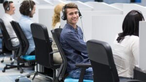 A row of call center agents busy working, except for one that is looking at the camera.